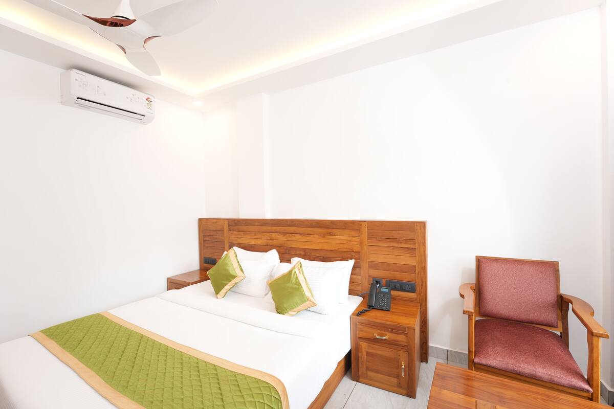 Una habitación de hotel con cama, mesita de noche, silla y aire acondicionado.