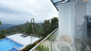 A rooftop pool with lounge chairs, a glass balustrade, and a view of a forested valley. - Zeezmount Resorts & Spa Munnar (Devikolam)