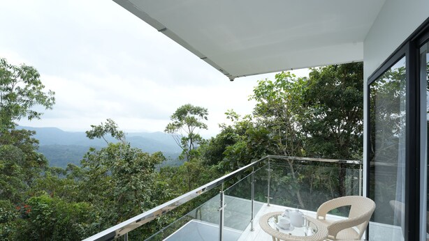 A balcony with a glass railing, wicker chairs, and a table with cups and saucers. - Zeezmount Resorts & Spa Munnar (Devikolam)