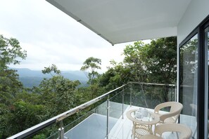 A balcony with a glass railing, wicker chairs, and a table with cups and saucers. - Zeezmount Resorts & Spa Munnar (Devikolam)