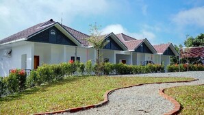 A row of white buildings with red-tiled roofs, surrounded by well-maintained greenery and a gravel pathway. - Zeezmount Resorts & Spa Munnar (Devikolam)