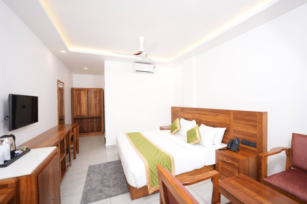 Habitación de hotel con cama, muebles de madera, escritorio, silla, televisor y ventilador de techo.