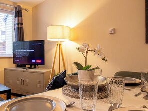 Hotelkamer met een televisie waarop Netflix staat, een lamp, een potorkidee en een eettafel gedekt met borden, glazen en bestek.
