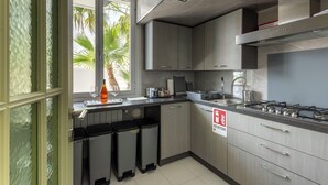 Una cocina moderna con armarios grises, estufa de acero inoxidable y ventana con vista a palmeras.