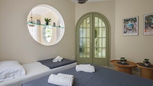 Un dormitorio con dos camas, un espejo redondo, una puerta verde y dos mesitas de noche con plantas.