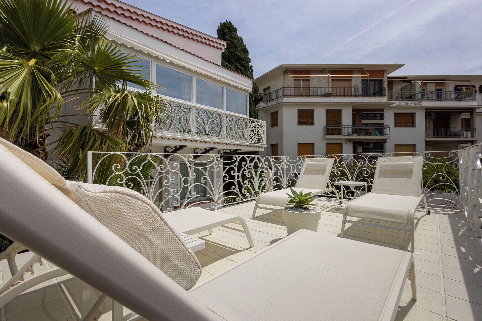 Een zonnig terras buiten met witte lounge fauteuils en een decoratieve metalen hek.
