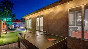An outdoor ping pong table with a paddle, surrounded by a patio area with a pool and lounge chairs. - Spacious 8-bedroom house in phenomenal Glendale with AC and gym (Glendale)