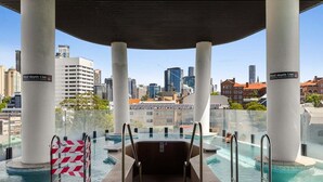 Una piscina infinita al aire libre con vistas a la ciudad, rodeada de columnas, y un cartel que indica una profundidad de 1,1m.