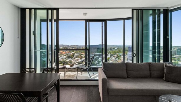 Una sala de estar moderna con un gran ventanal corredera que da a un balcón con vistas a la ciudad.
