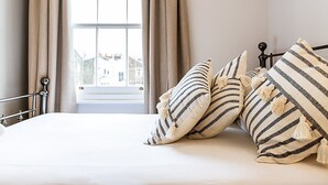 Una camera da letto con un letto, cuscini a righe, vista sugli edifici attraverso una finestra e tende.
