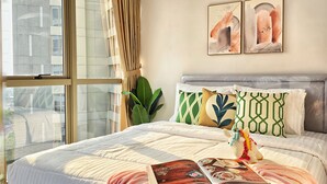 Ein modernes Schlafzimmer mit einem großen Bett, einem Fenster mit Vorhängen und zwei abstrakten Bildern an der Wand.