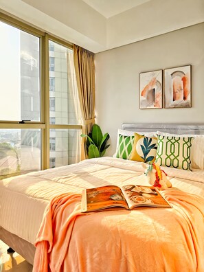 A modern bedroom with a large bed, a view of buildings through the window, and two abstract paintings on the wall. - Avenue By SanLiving - 2BR - HubLife Mall (Jakarta)