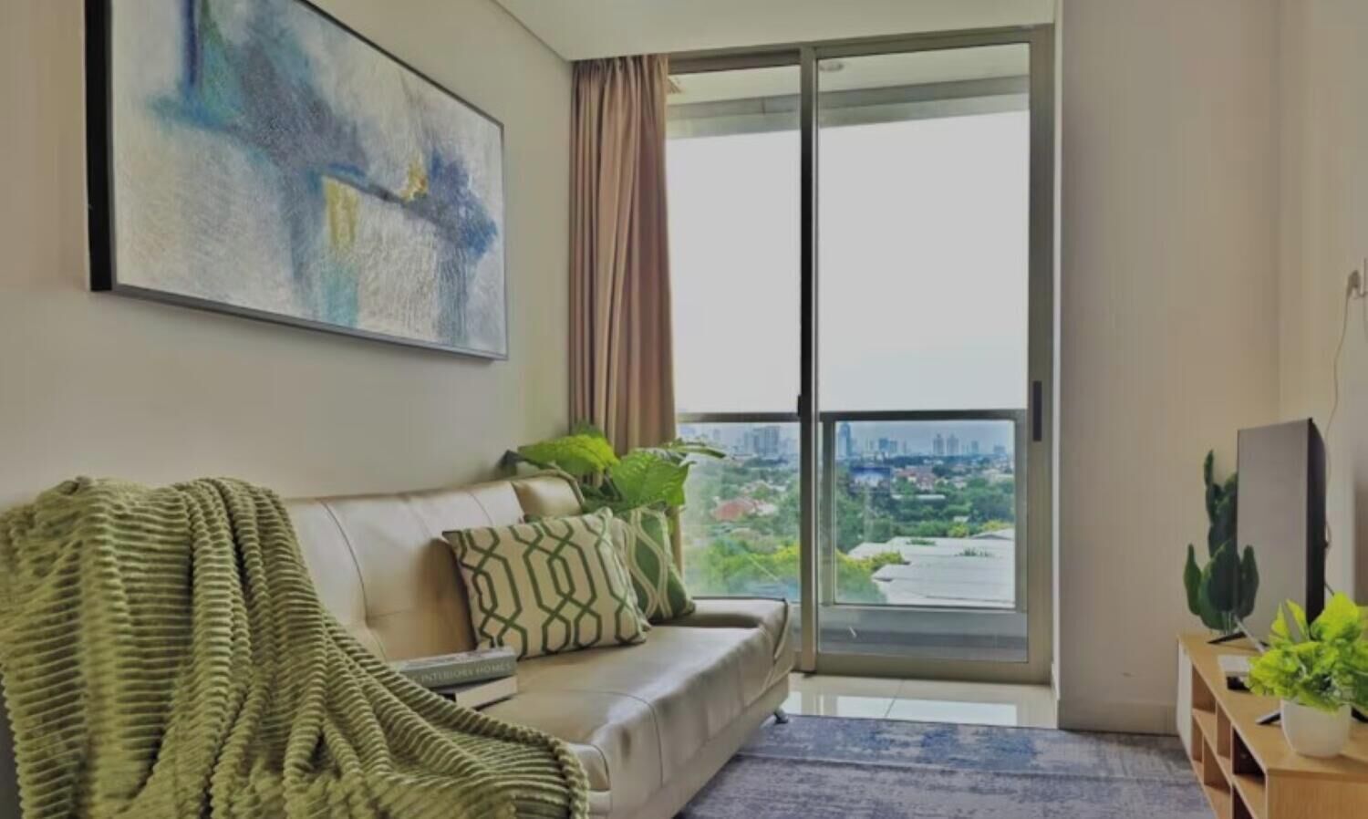 Una sala de estar con un sofá, una manta verde y vistas a la ciudad a través de la ventana.