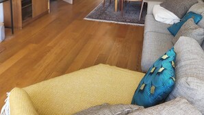 Ein geräumiges Wohnzimmer mit Holzboden, einer Couch mit gemusterten Kissen, einem Esstisch mit Stühlen, einer Chandelieber und einer Treppe zu einem anderen Raum.