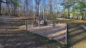 Ein Spielplatz mit Rutsche und Klettergerüsten, umgeben von Bäumen.