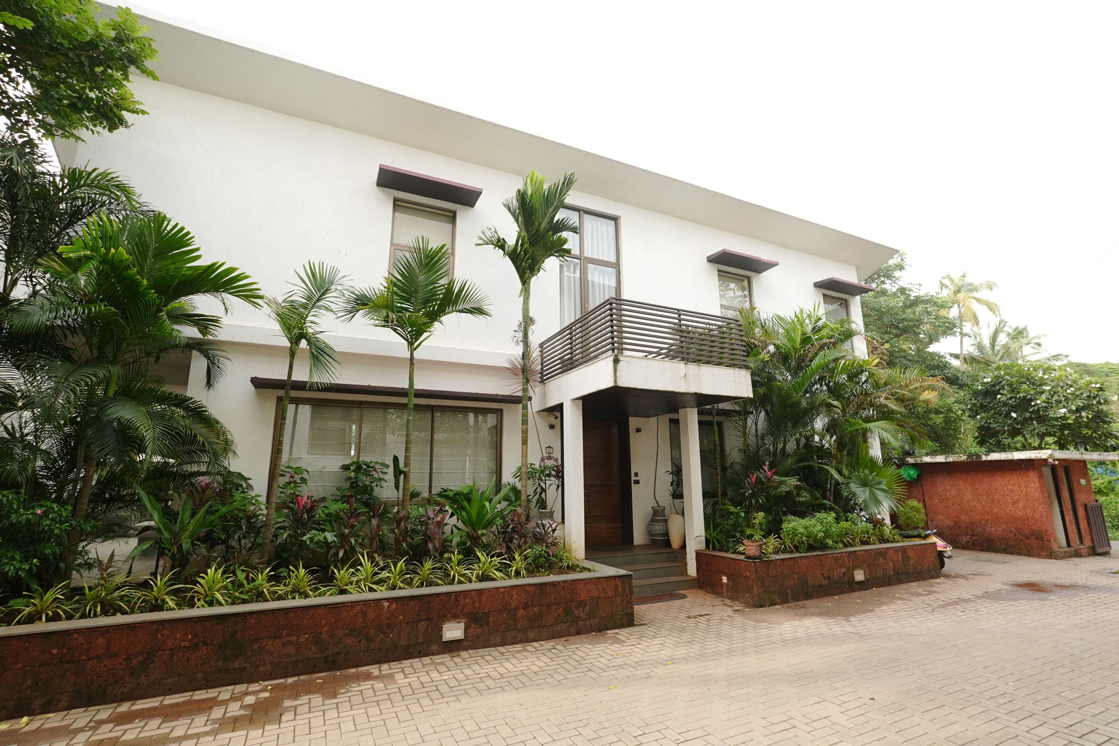 A modern two-story building with a balcony, surrounded by lush greenery and a paved walkway.