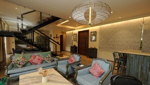 A spacious living area with a staircase, a bar area, and a seating arrangement with sofas and chairs. - Euphoria by Dia Hotels And Homes (Nerul)