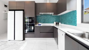 Eine moderne Küche mit grauen Schränken, einem weißen Kühlschrank, einem Einbauofen und einer türkisblauen Spritzschutzwand.