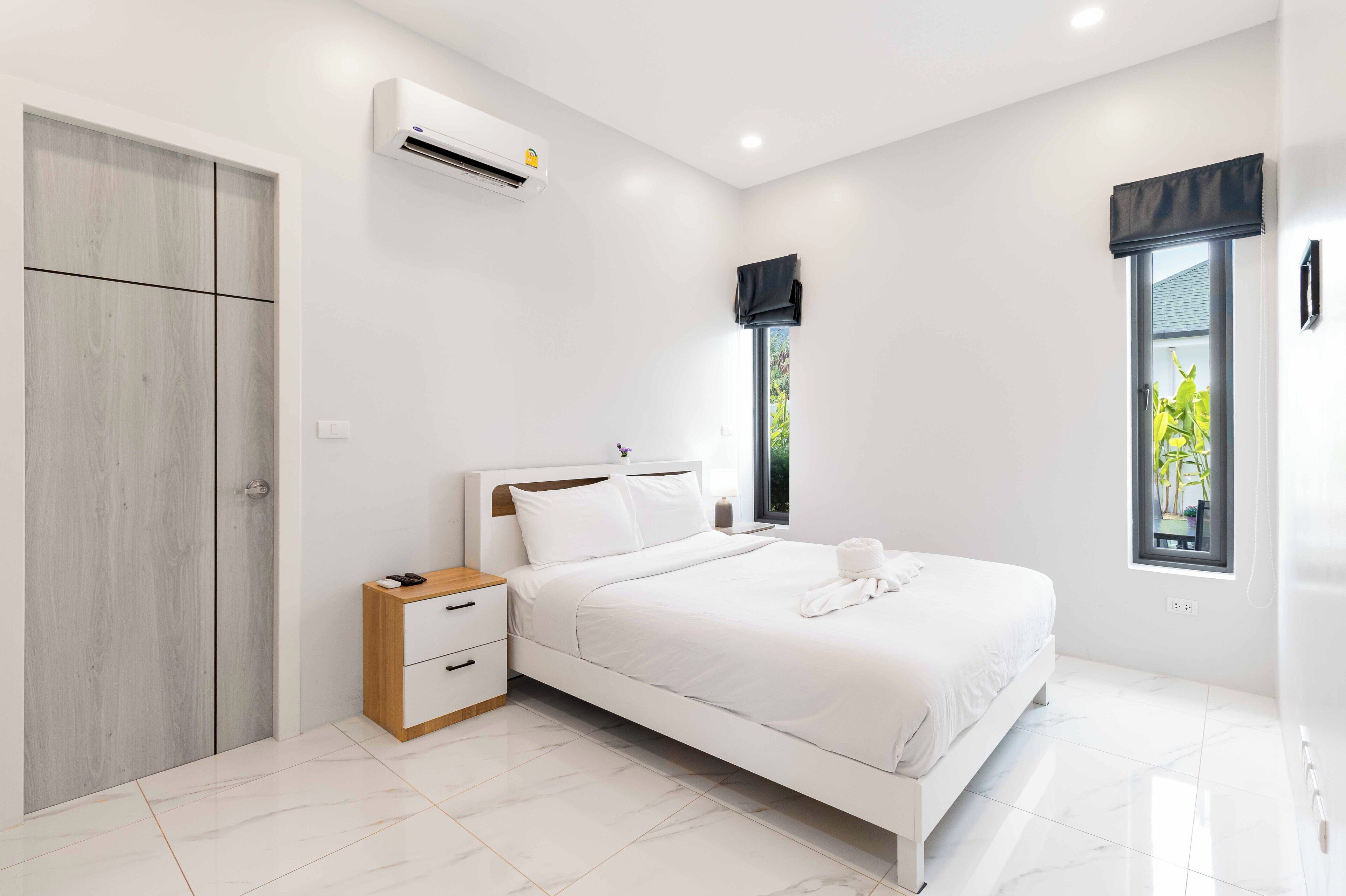 A modern bedroom with a bed, bedside table, wardrobe, and a window with a view of greenery.