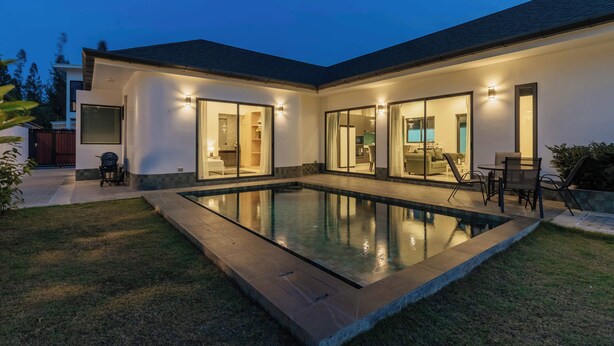 Ein modernes Haus mit Pool, großen Glasfenstern und Gartenmöbeln.