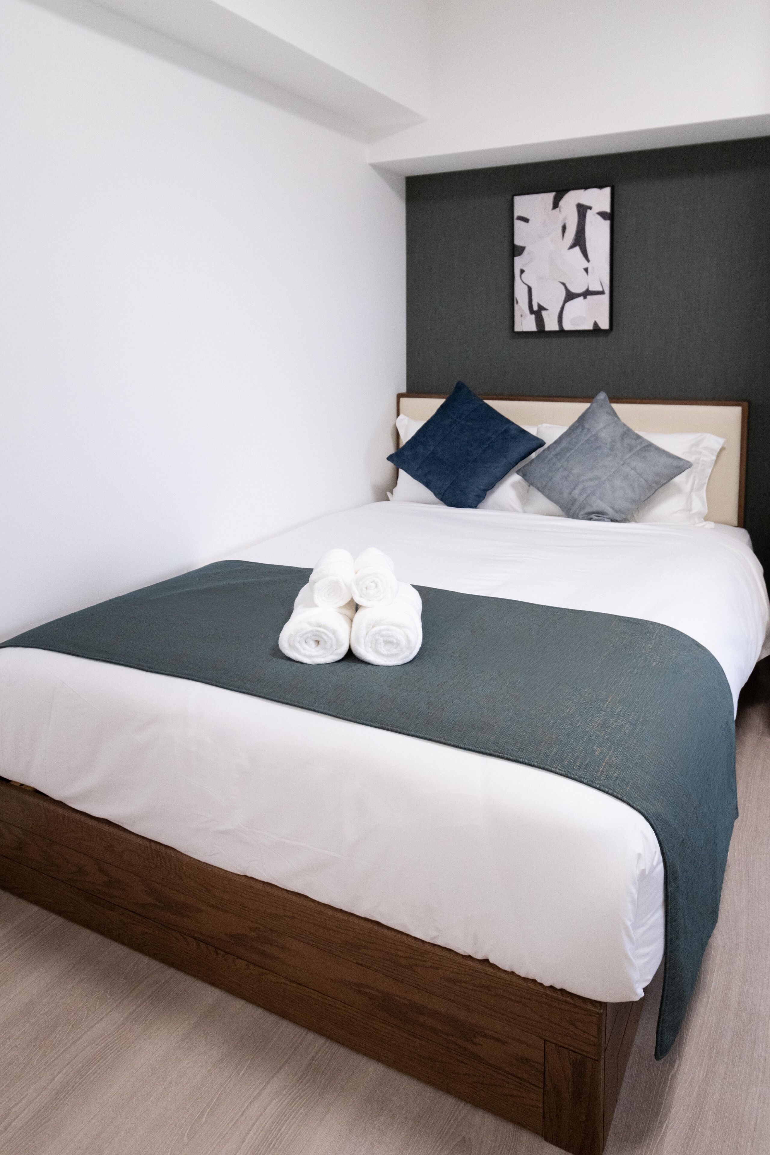 A neatly made bed with a dark green bedspread, white linens, and two rolled towels.