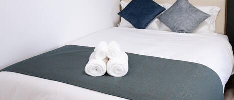 A neatly made bed with a dark green bedspread, white linens, and two rolled towels.
