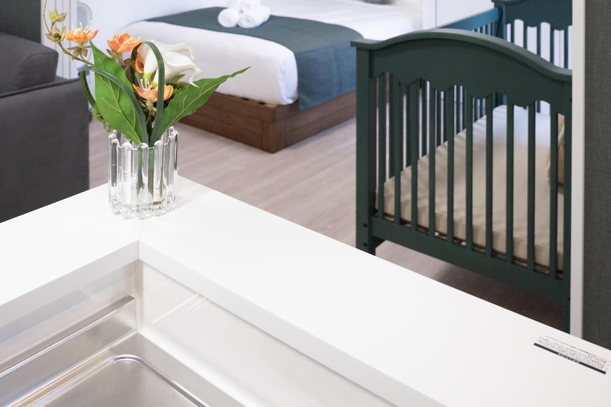 Quarto de hotel moderno com uma cama, um berço e uma pequena mesa com um vaso de flores.