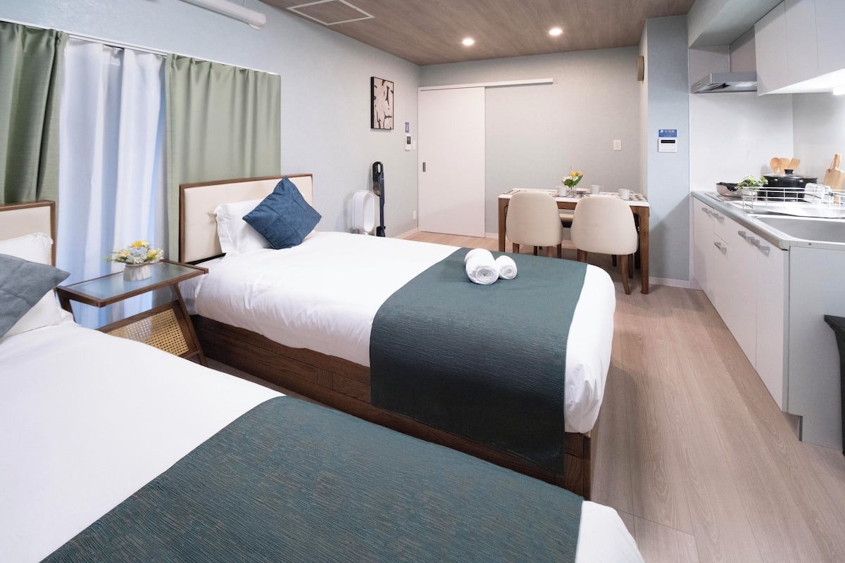 Quarto de hotel com duas camas, uma mesa de jantar e uma cozinha compacta.