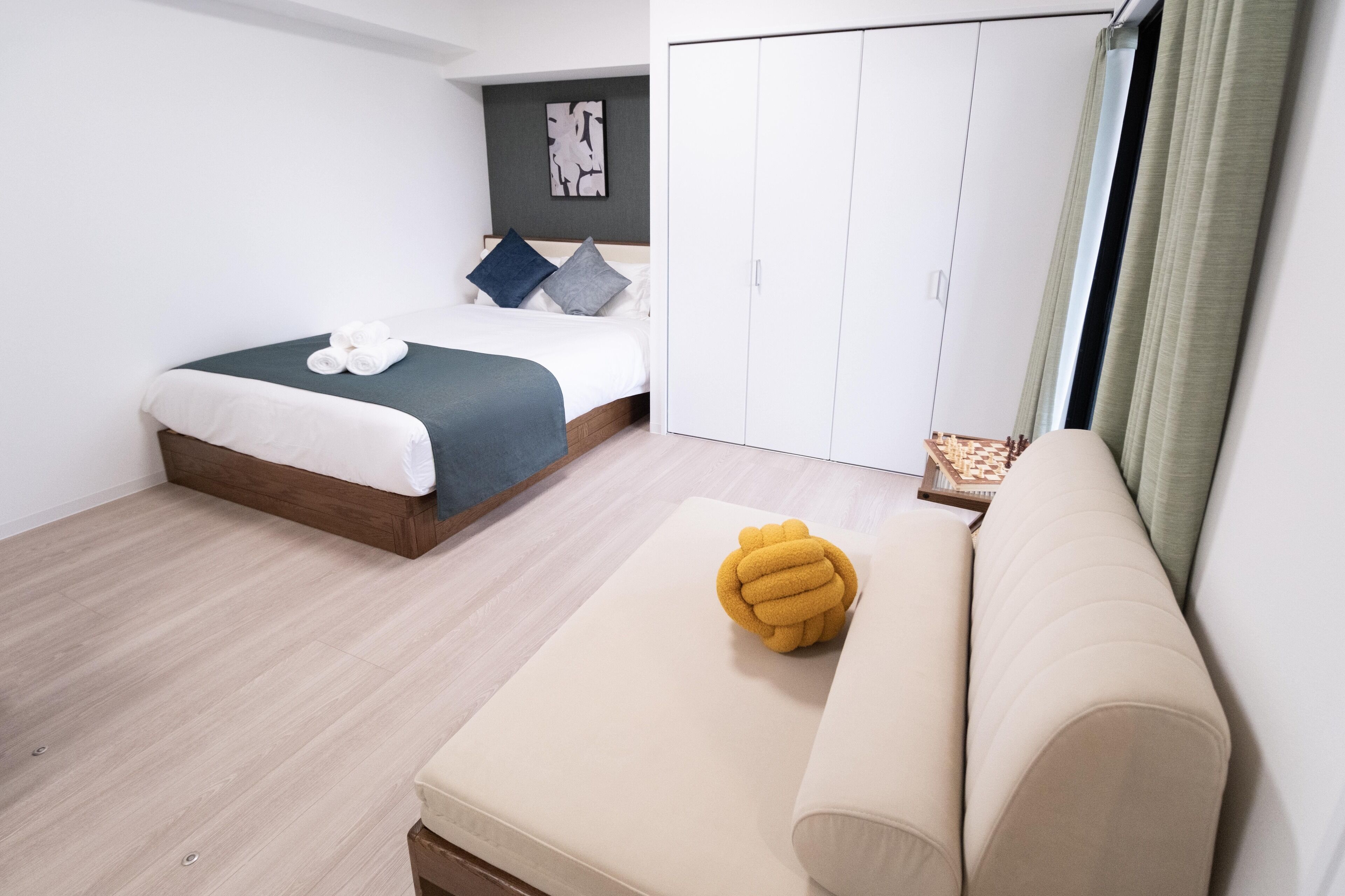 Un dormitorio moderno con cama, sofá, armario y una mesita con un tablero de ajedrez.