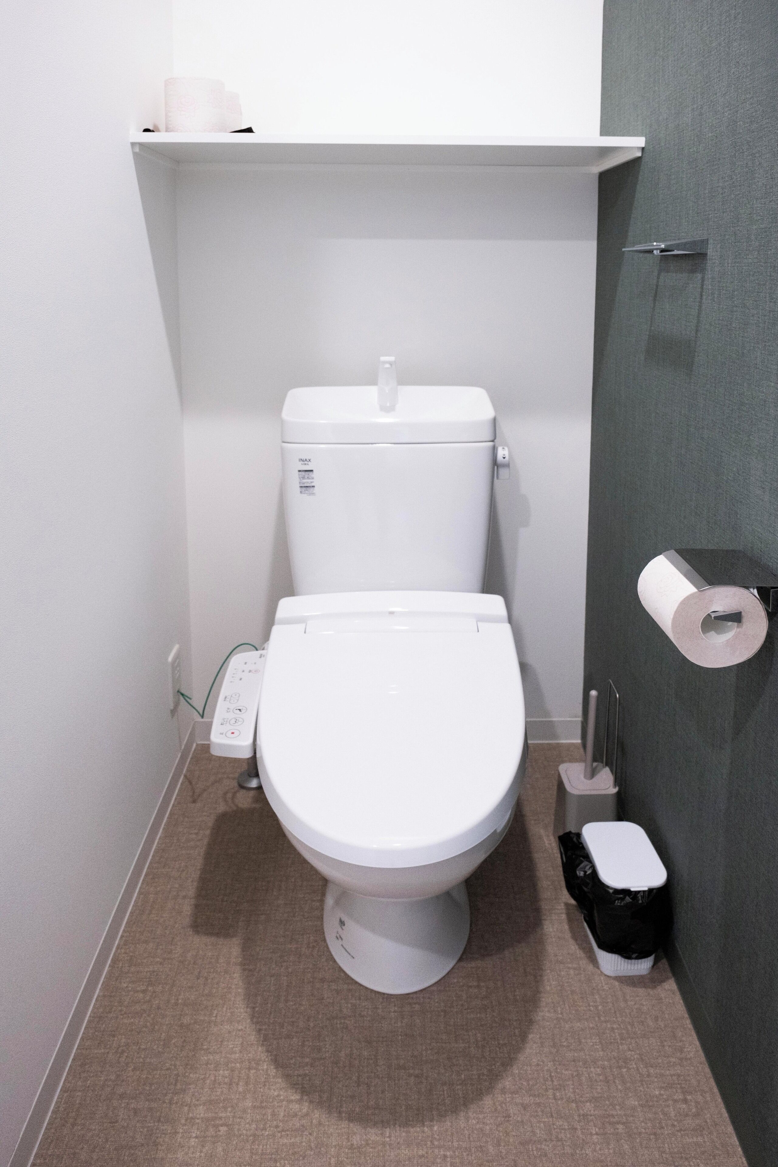 A compact bathroom with a white toilet, a paper towel dispenser, and a trash bin.