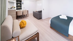 A modern hotel room with a sofa, a bed, a desk with chairs, a small kitchenette, and a sliding door. - The Peak Bentencho (Osaka)