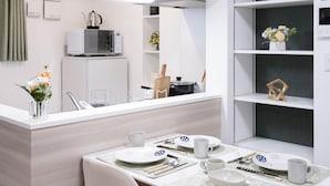 A modern kitchen with a built-in microwave, a small refrigerator, and a dining area with a table set for two. - The Peak Bentencho (Osaka)