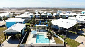 Un resort con varios edificios azules y blancos, una piscina central y vistas a la playa y el océano.