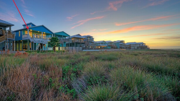 Una propiedad frente a la playa con varias casas, una escalera destacada y vista al océano al atardecer.