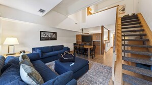 Una sala de estar moderna con un conjunto de sofá azul, un comedor y una escalera.