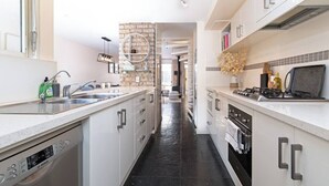 A modern kitchen with white cabinetry, a Bosch dishwasher, a stove, and a large window providing natural light. - Character & Charm 3BR home - free wine (Adelaide)