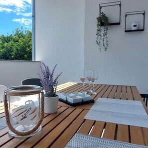 A wooden table with a glass jar, a potted plant, and two wine glasses on a balcony with a view of trees and a clear sky. - Ugodan apartman sa prekrasnom terasom u mirnoj ulici u blizini plaže (Vodice)