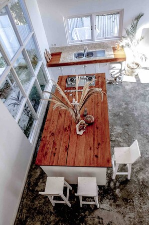 Eine Küche mit einem Holztisch, zwei weißen Stühlen, einem Fenster und einer Spüle.