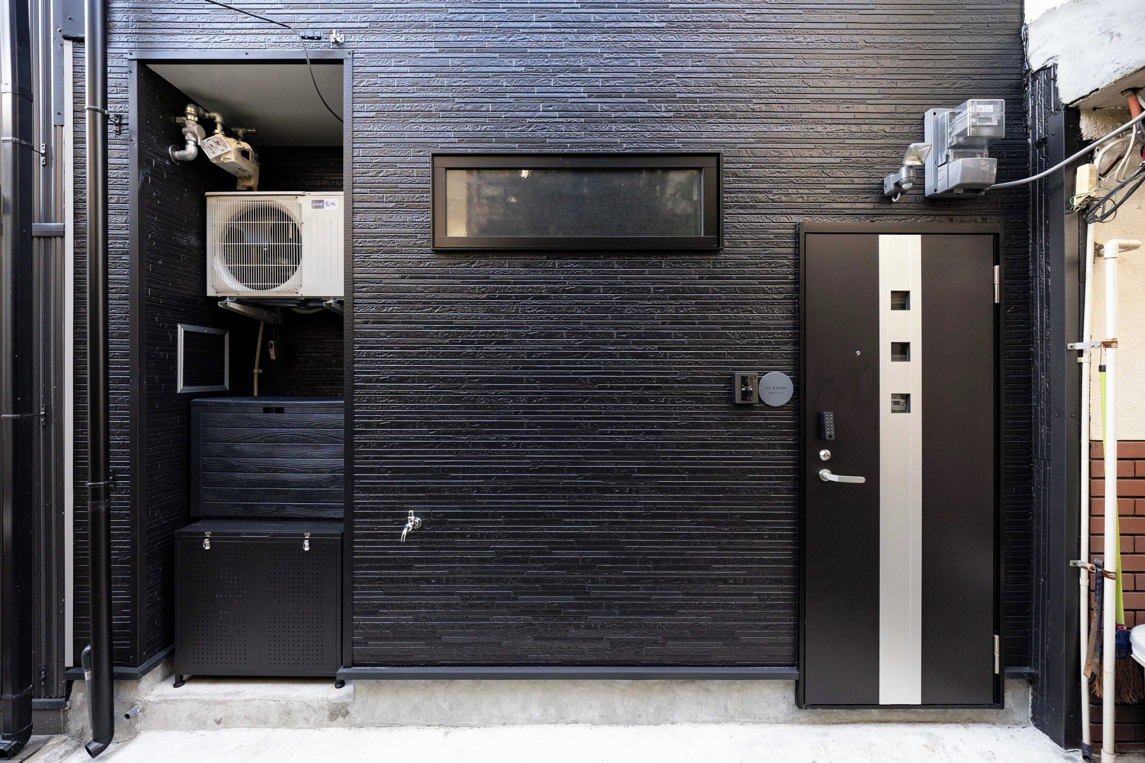 A modern building exterior with a black textured wall, a large air conditioning unit, and a door with a vertical stripe.