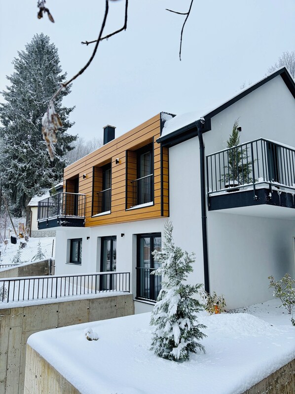 Una casa moderna de dos pisos con fachada de madera, ventanas grandes y un balcón.
