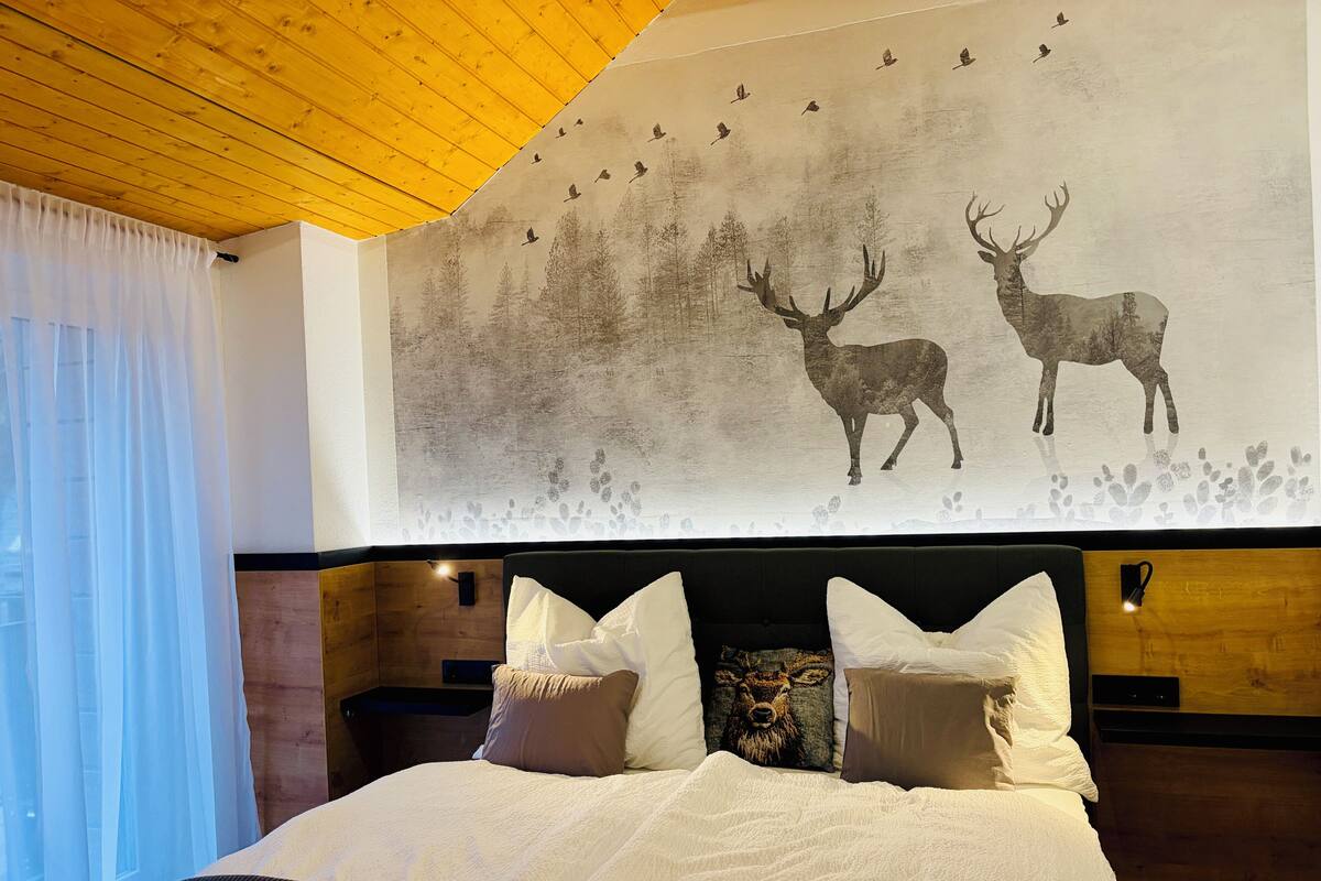 Ein Schlafzimmer mit einem großen Bett, einem Holzkopfende und einer Wandmalerei von Hirschen und Vögeln.
