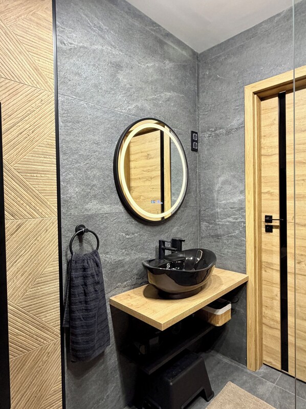 A modern bathroom with a round mirror, wooden vanity, and a towel rack.