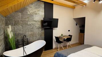 Un dormitorio moderno con pared de piedra, bañera independiente, cama, escritorio y televisor.