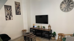 Un salon moderne avec une grande horloge murale, un téléviseur à écran plat et une table basse en bois.