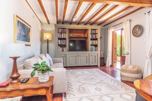 Ein gemütliches Wohnzimmer mit einer Couch, einem Couchtisch mit Pflanze, einem Fernseher und Bücherregalen voller Bücher.