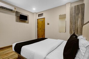A hotel room with a bed, a wooden door, a mounted TV, and a mirror on the wall. - Collection O BKC Kurla Formerly Hotel Pride Suite (Mumbai)