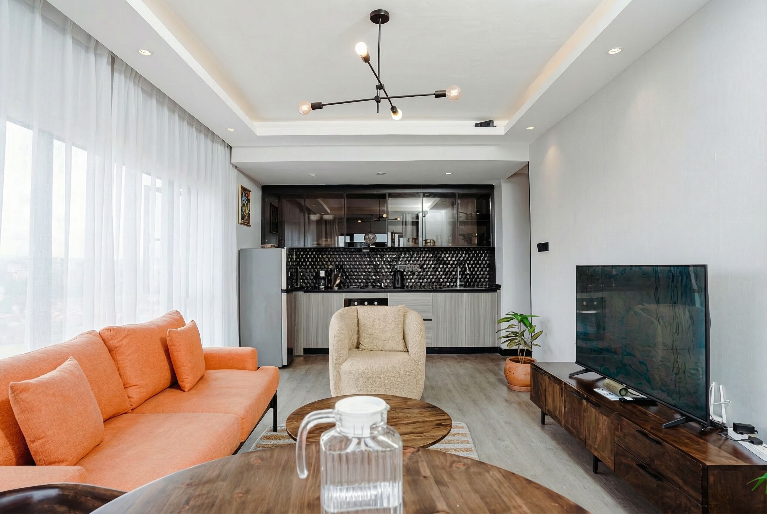 Ein modernes Wohnzimmer mit Sofa, Couchtisch und Fernseher. Im Hintergrund ist eine Küche zu sehen.