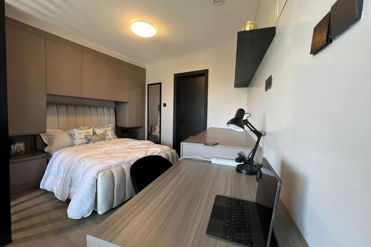 Habitación de hotel moderna con cama, escritorio, ordenador portátil, lámpara de escritorio y mesita de noche con teléfono.