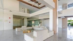 A spacious, modern lobby with a high ceiling, a glass elevator, and a seating area with white sofas and a glass coffee table. - Cozy and Nature-Inspired Studio Unit (Lapu-Lapu)