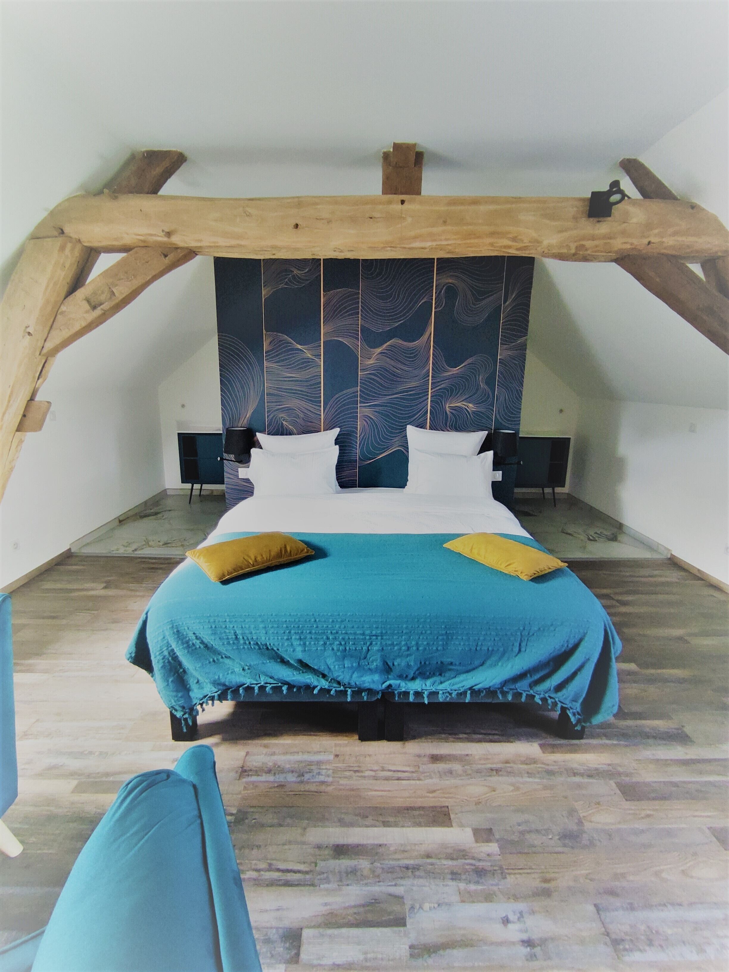 Un dormitorio con techo inclinado, una cama con colcha azul y amarilla, dos almohadas y cabecero de madera con diseño de olas.